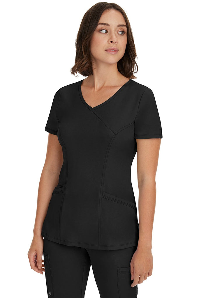A young woman wearing a Women's Madison Mock Wrap Scrub Top from HH Works in Black featuring a medium center back length of 24".