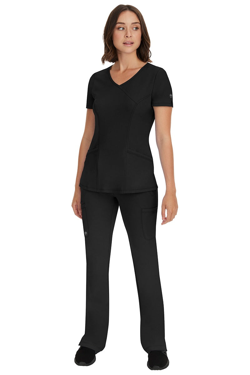 A female LVN wearing an HH-Works Women's Madison Mock Wrap Scrub Top in Black featuring a super comfortable fabric made of 91% polyester & 9% spandex.