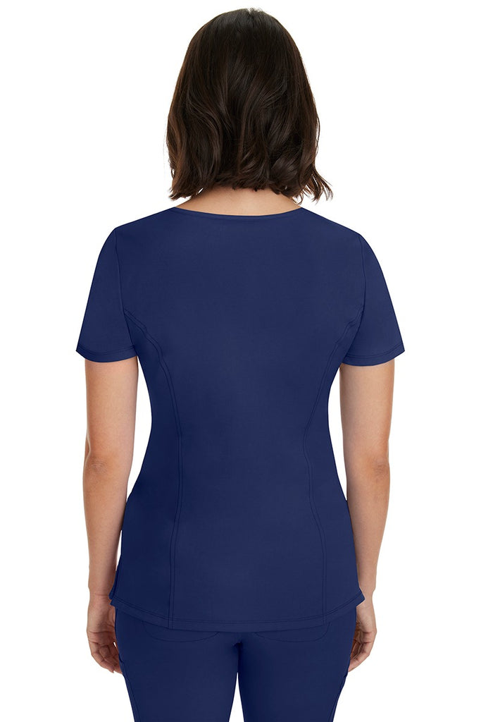 A young woman wearing a HH-Works Women's Madison Mock Wrap Scrub Top in Navy featuring princess seams throughout.
