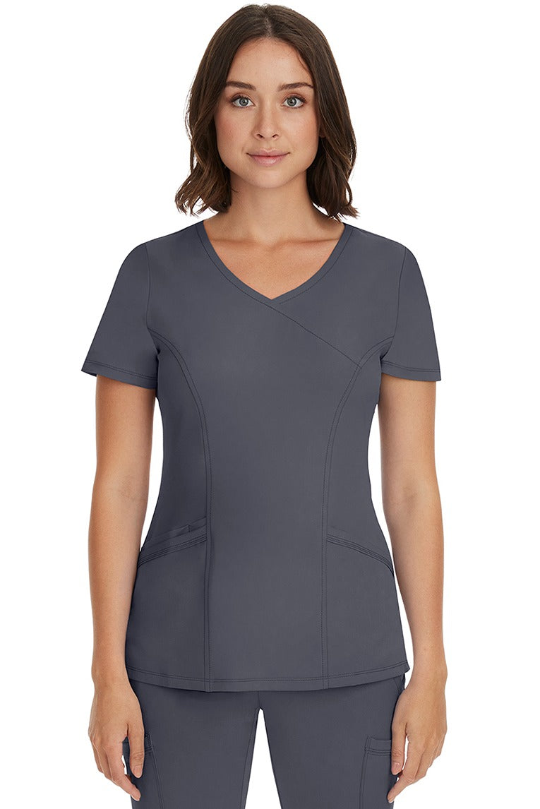 A young female Registered Nurse wearing an HH-Works Women's Madison Mock Wrap Scrub Top in Pewter featuring a faux wrap neckline.