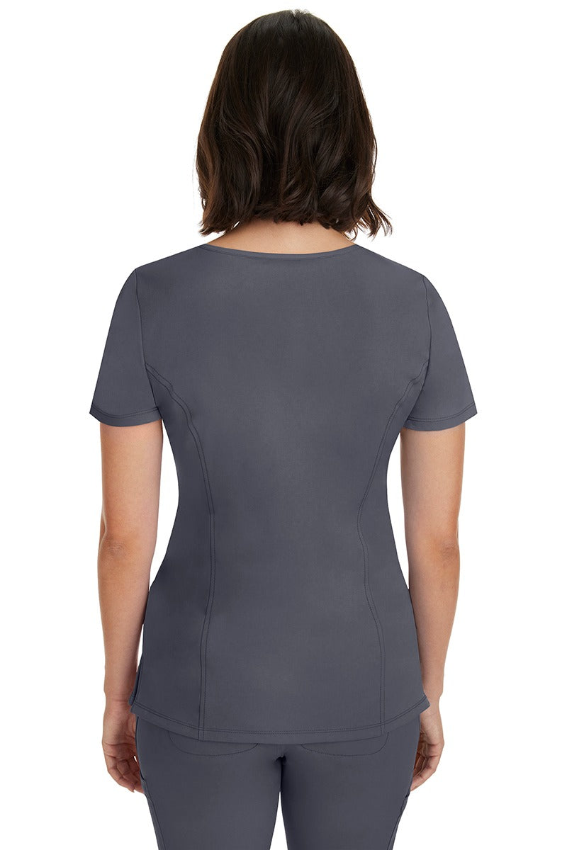 A young woman wearing a HH-Works Women's Madison Mock Wrap Scrub Top in Pewter featuring princess seams throughout.