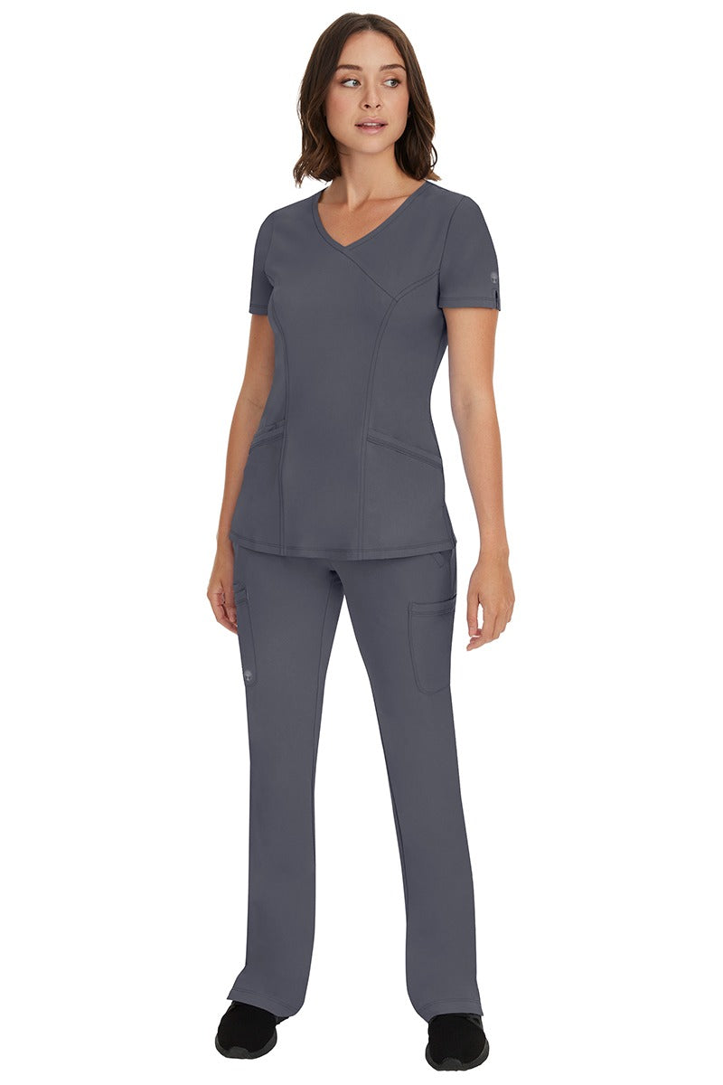 A female LVN wearing an HH-Works Women's Madison Mock Wrap Scrub Top in Pewter featuring a super comfortable fabric made of 91% polyester & 9% spandex.