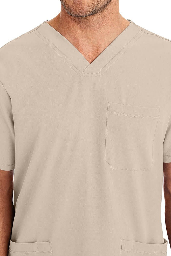 A young male CNA wearing an HH-Works Men's Matthew V-Neck Scrub Top in Khaki featuring a single chest pocket on the wearer's left side.