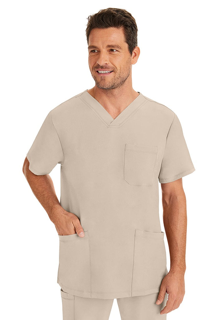 A male healthcare professional wearing an HH-Works Men's Matthew V-Neck Scrub Top in Khaki featuring a total of 4 pockets. for all your on the job storage needs.