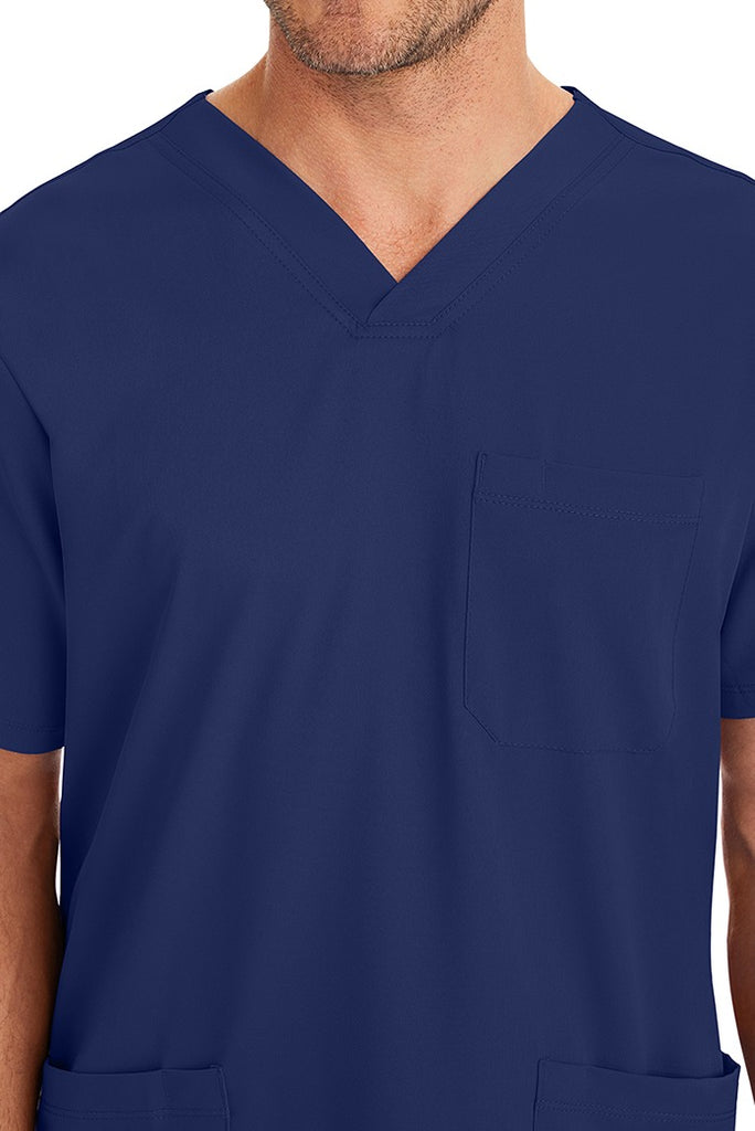 A young male CNA wearing an HH-Works Men's Matthew V-Neck Scrub Top in Navy featuring a single chest pocket on the wearer's left side.