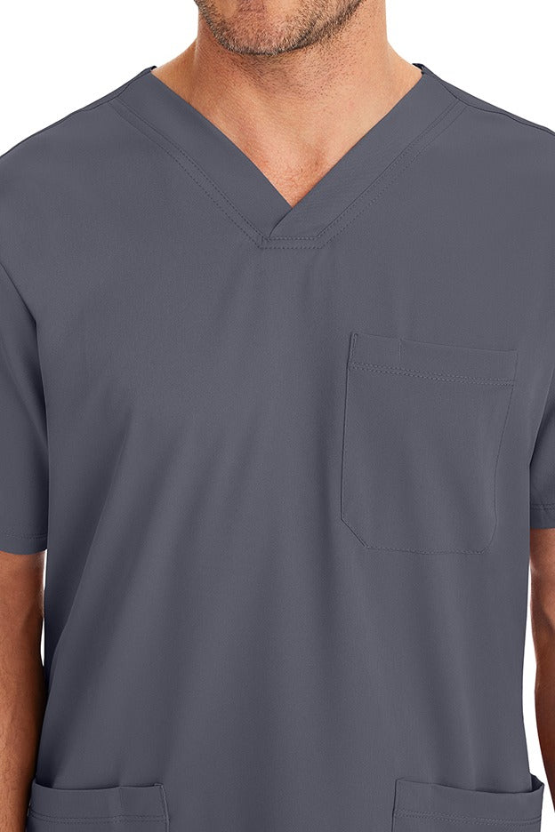 A young male CNA wearing an HH-Works Men's Matthew V-Neck Scrub Top in Pewter featuring a single chest pocket on the wearer's left side.