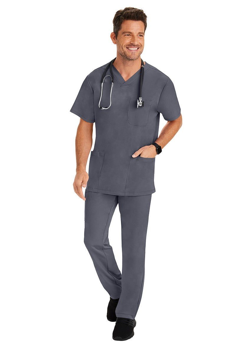 A young male Home Care Registered Nurse wearing an HH-Works Men's Matthew V-Neck Scrub Top in Pewter featuring a fade resistant fabric to ensure a long-lasting comfortable fit.