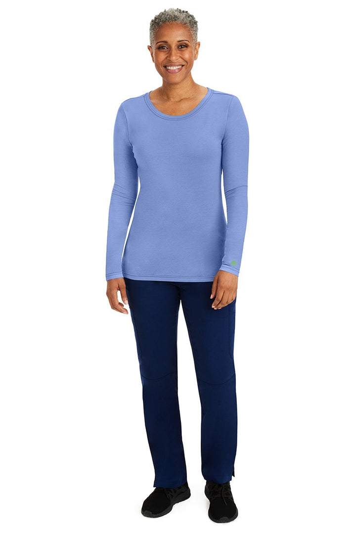 A female nurse wearing a Purple Label Women's Melissa Long Sleeve T-Shirt from Healing Hands in Ceil featuring a banded crew neckline.