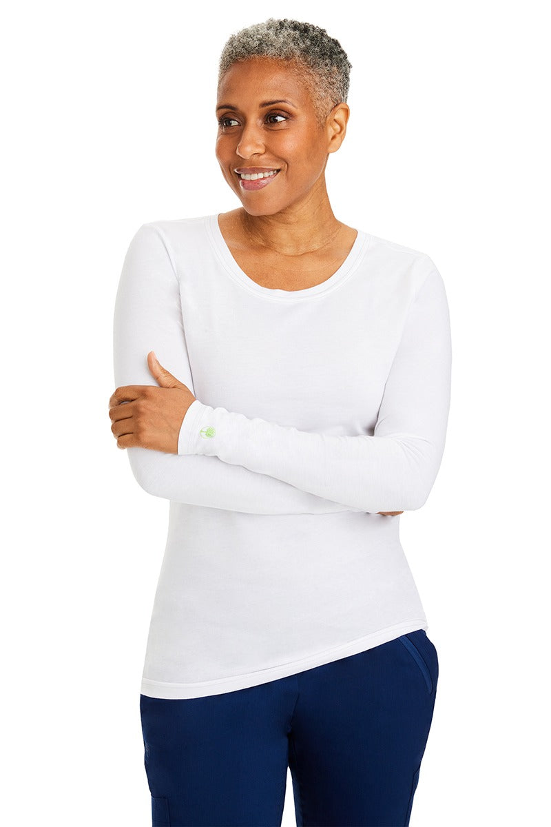 A female nurse wearing a Purple Label Women's Melissa Long Sleeve T-Shirt from Healing Hands in White featuring a banded crew neckline.