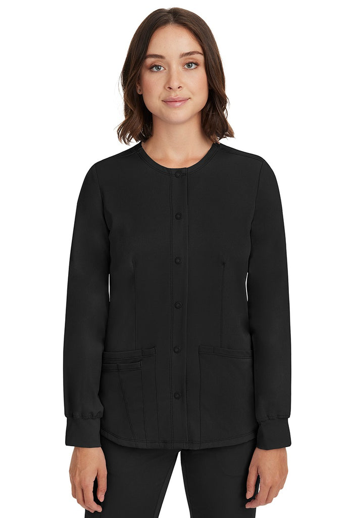 A young female nurse wearing a Women's Megan Snap Front Scrub Jacket from HH Works in Black featuring a round neckline & long sleeves.