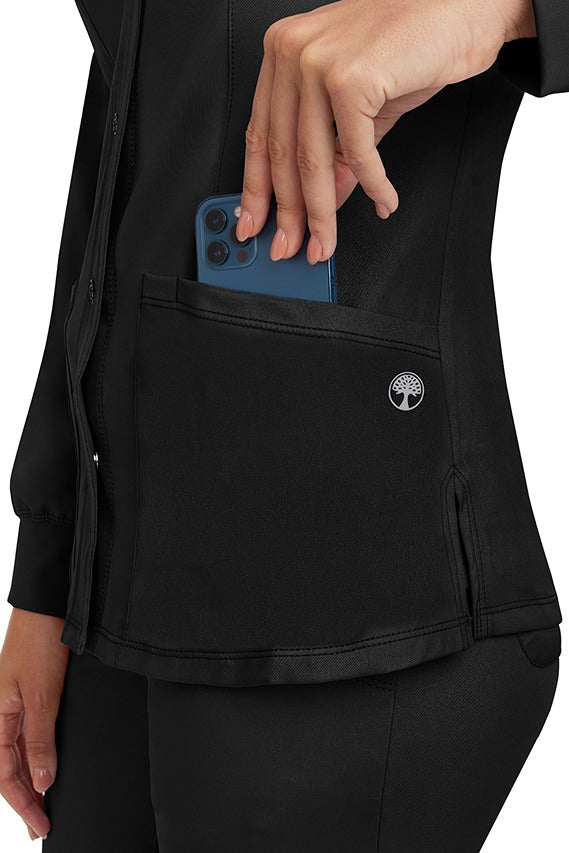 A young lady wearing an HH-Works Women's Megan Snap Front Scrub Jacket in Black featuring two front patch pockets.