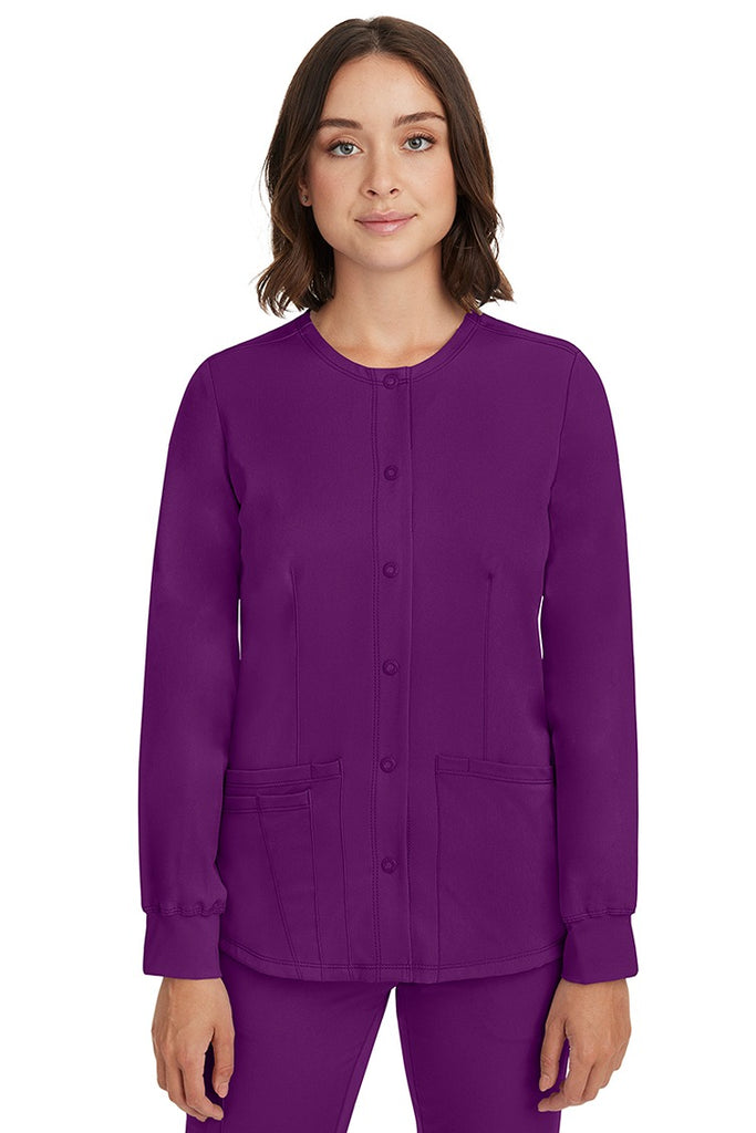 A young female nurse wearing a Women's Megan Snap Front Scrub Jacket from HH Works in Eggplant featuring a round neckline & long sleeves.