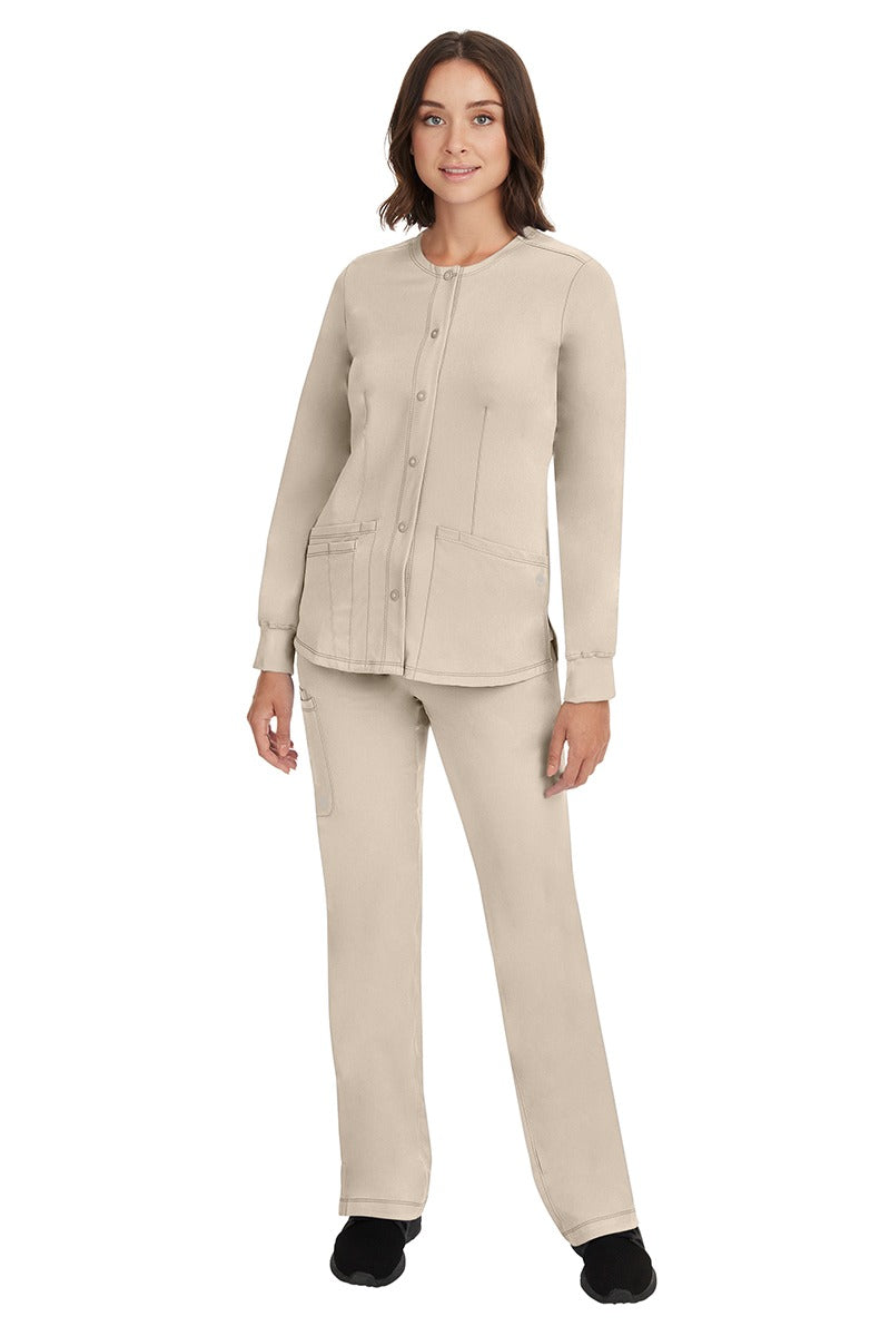 A young female Home Care Registered Nurse wearing an HH-Works Women's Megan Snap Front Scrub Jacket in Khaki featuring yoga knit cuffs to ensure a flattering and comfortable fit.