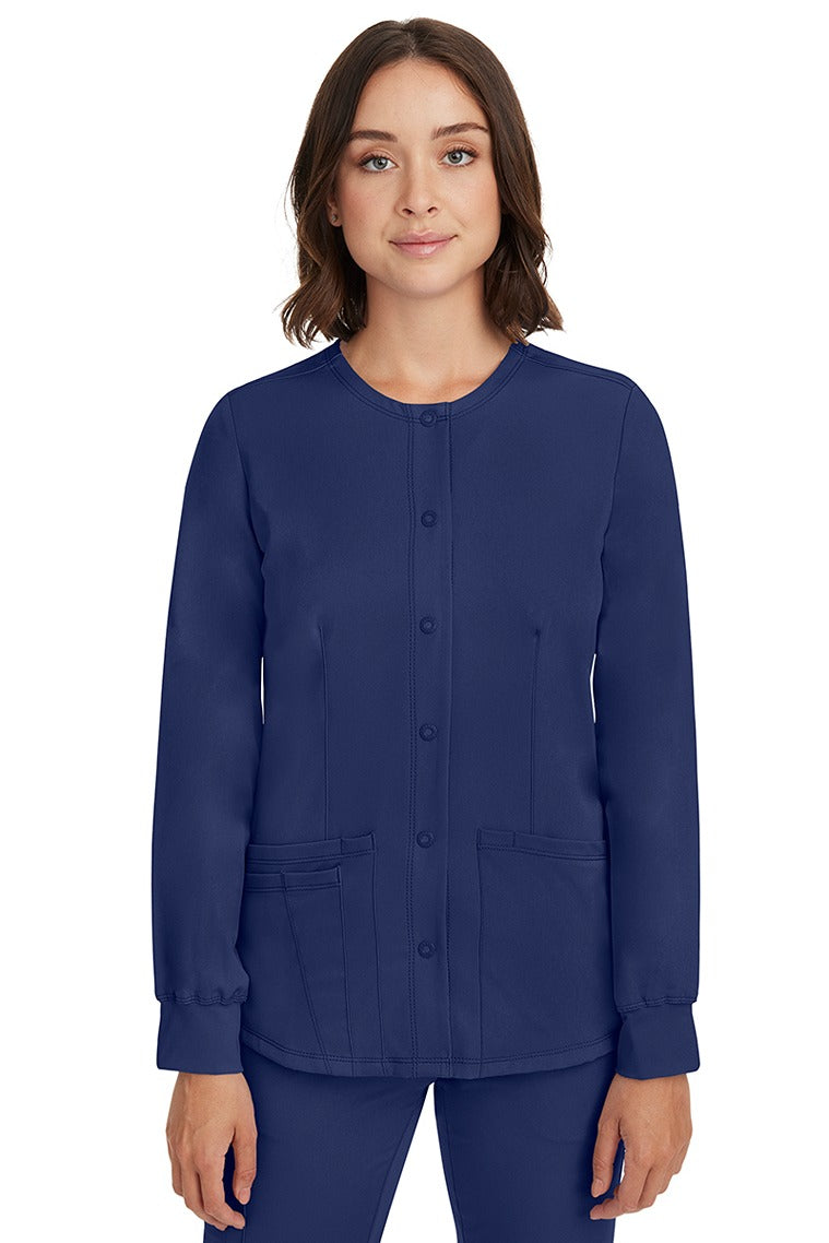 A young female nurse wearing a Women's Megan Snap Front Scrub Jacket from HH Works in Navy  featuring a round neckline & long sleeves.