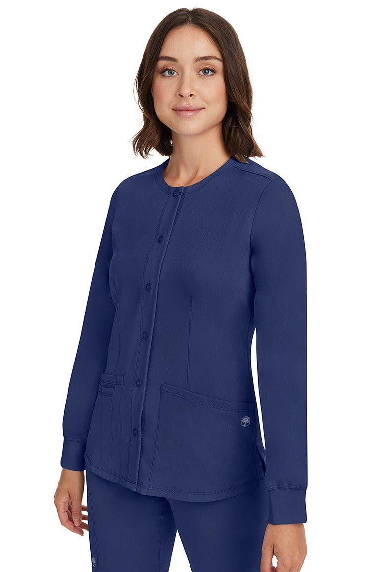 A young female CNA wearing an HH-Works Women's Megan Snap Front Scrub Jacket in Navy featuring side slits for additional range of motion.