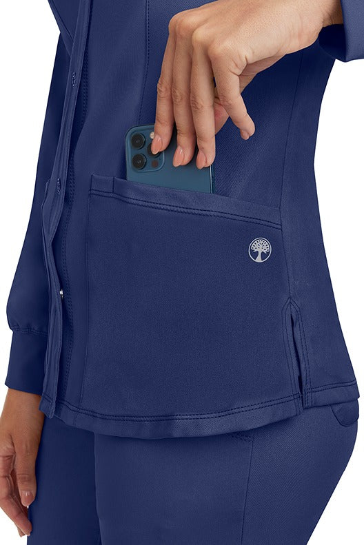 A young lady wearing an HH-Works Women's Megan Snap Front Scrub Jacket in Khaki  featuring two front patch pockets.