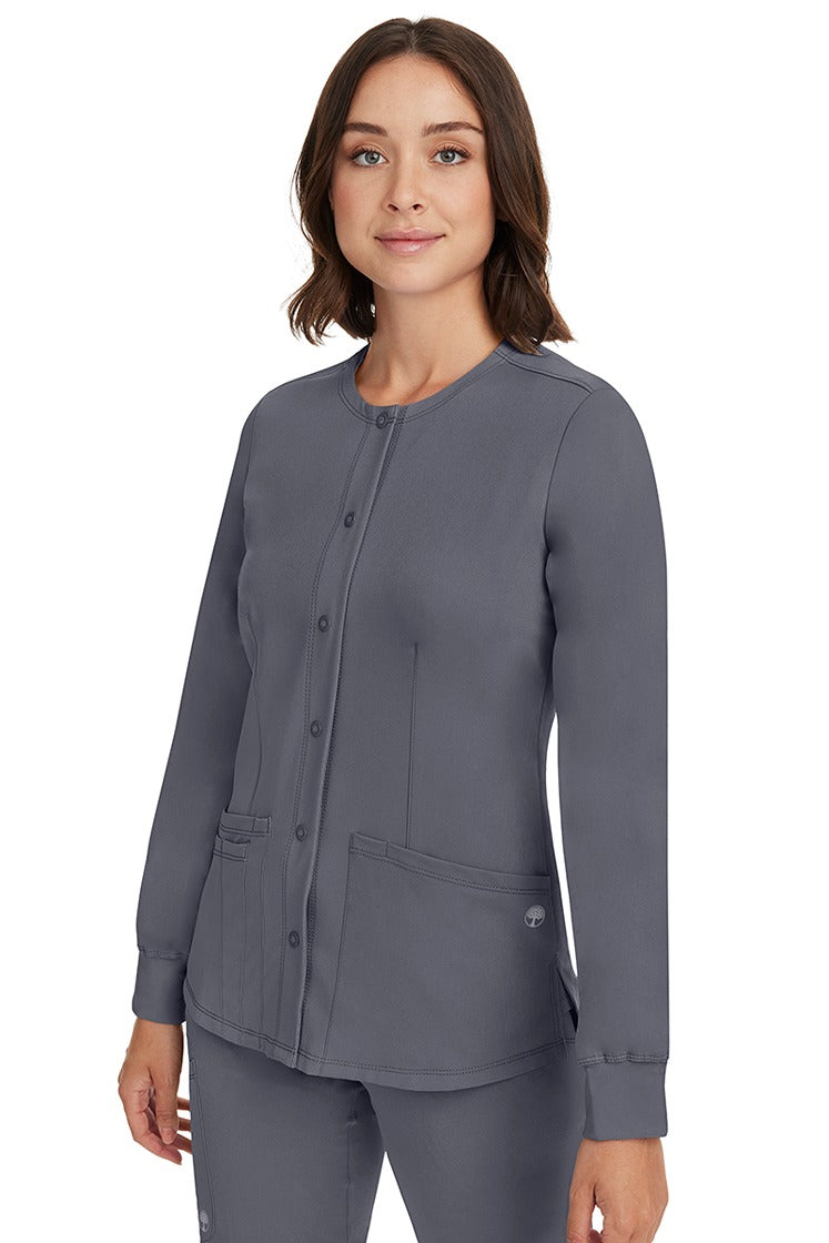 A young female CNA wearing an HH-Works Women's Megan Snap Front Scrub Jacket in Pewter featuring side slits for additional range of motion.