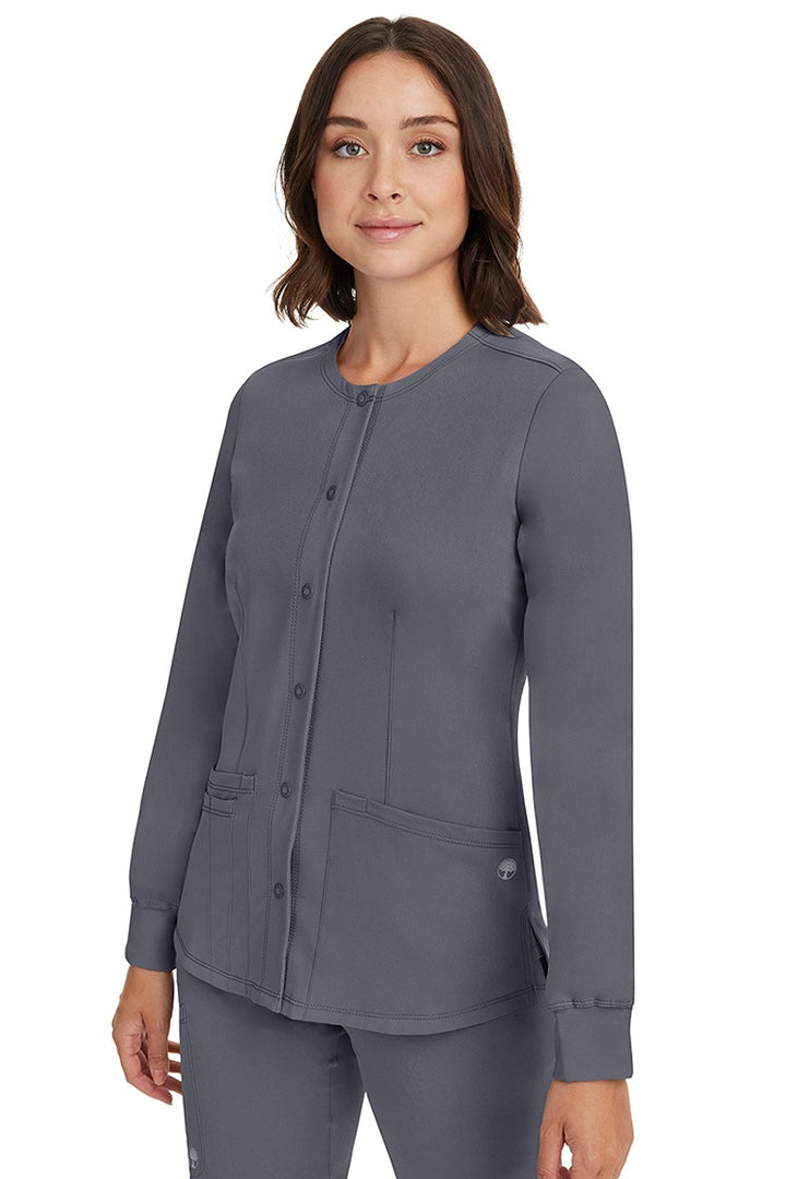 A young female CNA wearing an HH-Works Women's Megan Snap Front Scrub Jacket in Pewter featuring side slits for additional range of motion.