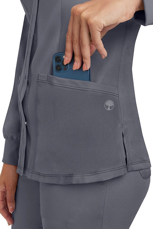 A young lady wearing an HH-Works Women's Megan Snap Front Scrub Jacket in Pewter featuring two front patch pockets.