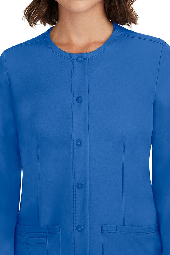 A female LPN wearing a Women's Megan Snap Front Scrub Jacket from HH Works in Royal featuring a snap-up button front closure.