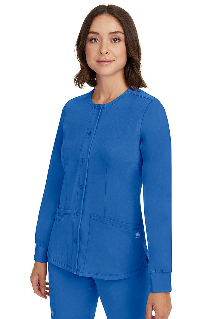 A young female CNA wearing an HH-Works Women's Megan Snap Front Scrub Jacket in Royal featuring side slits for additional range of motion.