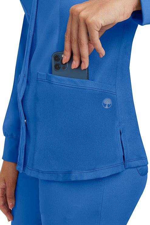 A young lady wearing an HH-Works Women's Megan Snap Front Scrub Jacket in Royal featuring two front patch pockets.