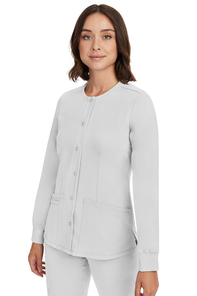 A young female CNA wearing an HH-Works Women's Megan Snap Front Scrub Jacket in White featuring side slits for additional range of motion.