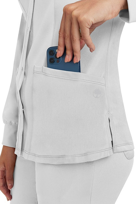 A young lady wearing an HH-Works Women's Megan Snap Front Scrub Jacket in White featuring two front patch pockets.