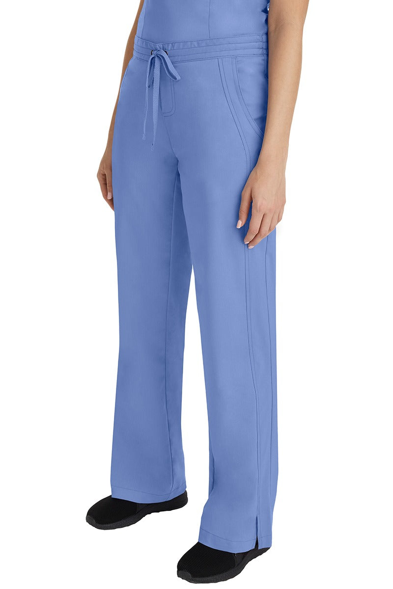 A young Home Care Registered Nurse wearing a Purple Label Women's Taylor Drawstring Scrub Pant in Ceil featuring front wrap seaming detail throughout.