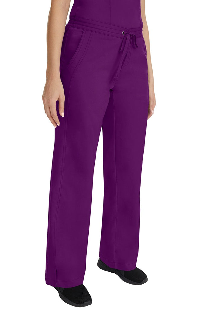 A young female RN wearing the Purple Label Women's Taylor Drawstring Scrub Pant in Eggplant featuring side slits at the ankle for easy slip-on or removal.