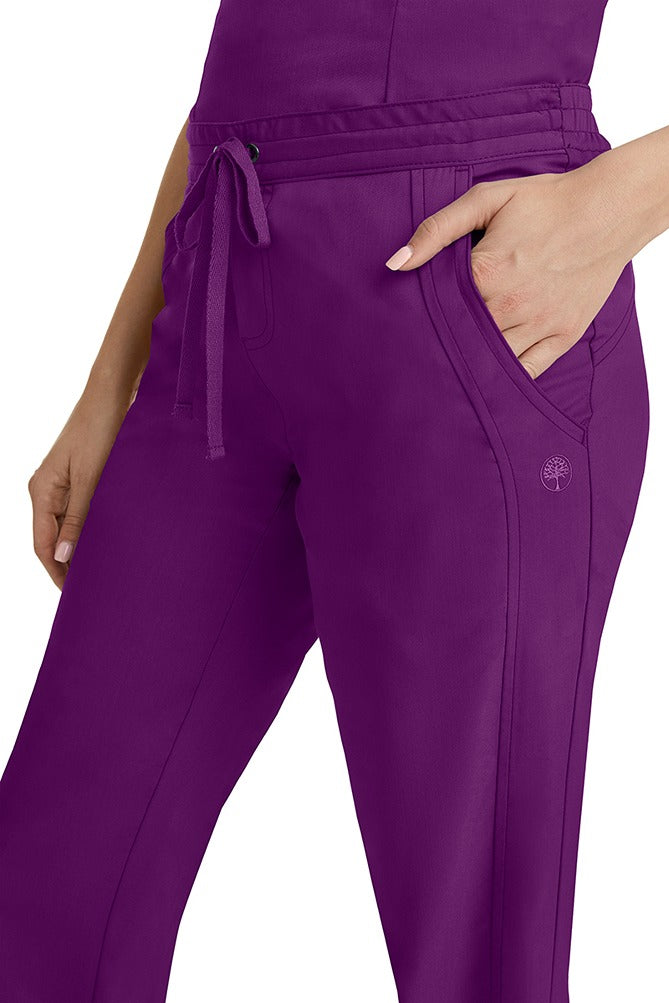 A young woman wearing a pair of Purple Label Women's Taylor Drawstring Scrub Pants from Healing Hands in Eggplant. Perfect for Healthcare Professionals working in Hospitals, Doctors offices, Dental Groups & Veterinary offices!
