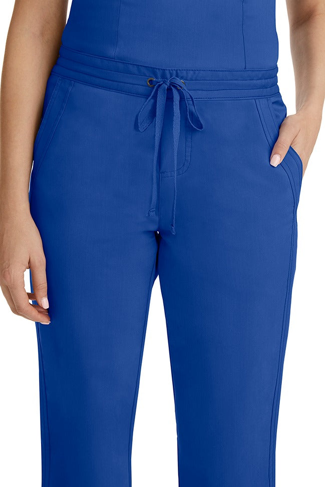 A female healthcare professional wearing a Purple Label Women's Taylor Drawstring Scrub Pant in Galaxy Blue featuring triple needle stitching throughout.