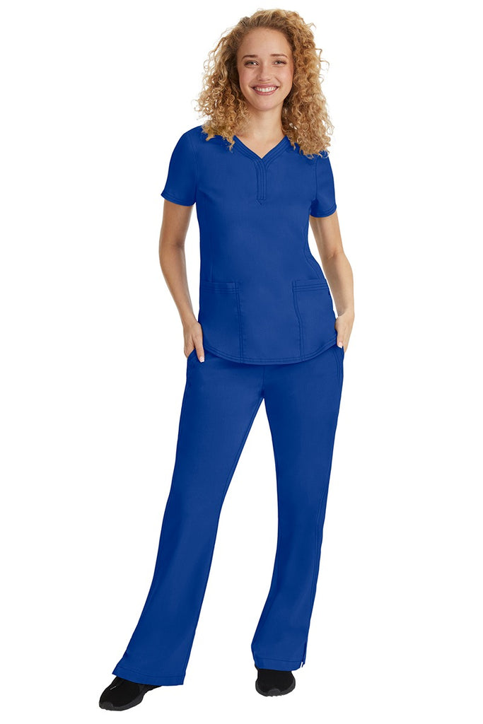 A young female nurse wearing a Purple Label Women's Taylor Drawstring Scrub Pant from Healing Hands in Galaxy Blue featuring a fabric that resists wrinkles, shrinking & fading better than traditional cotton scrubs.