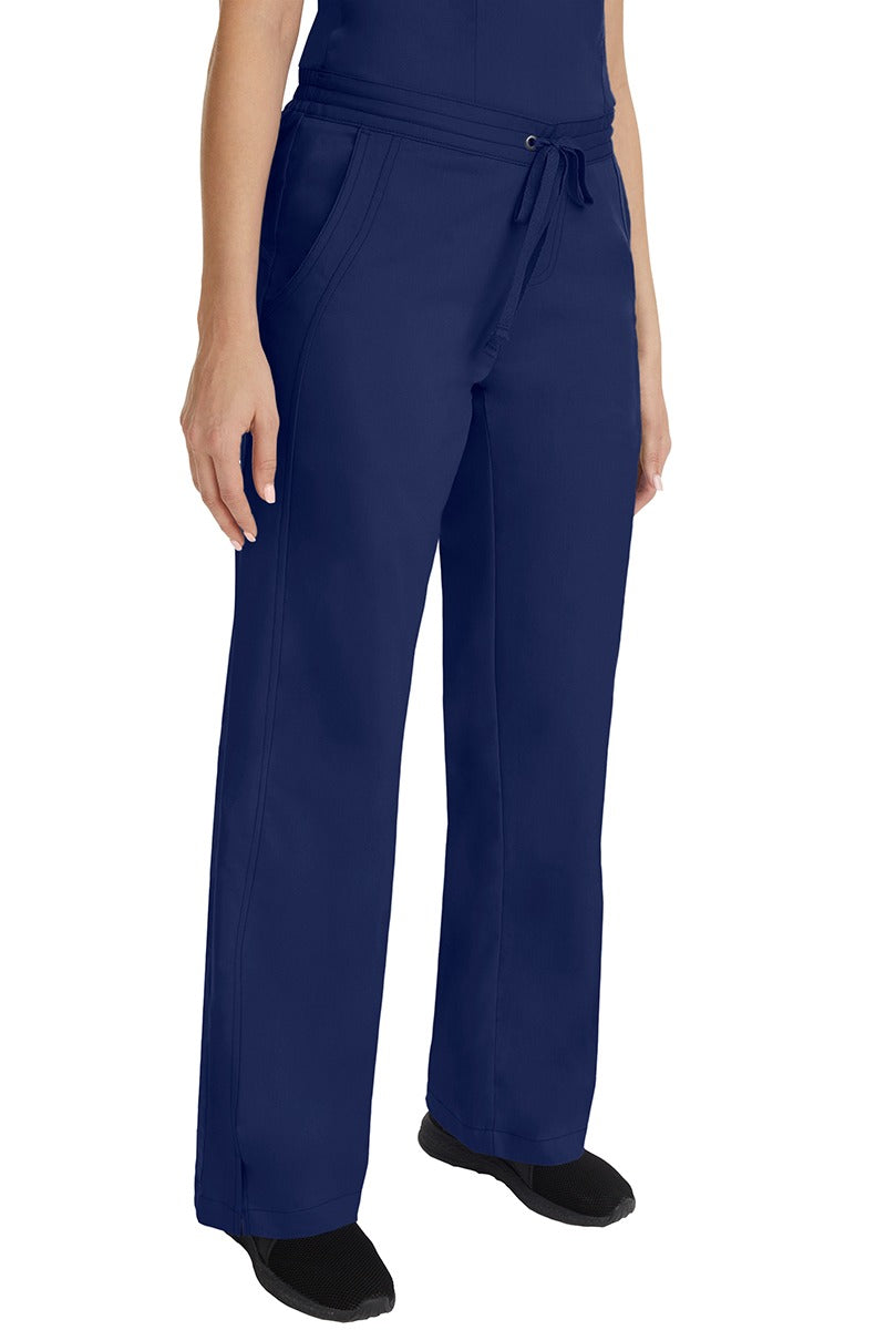 A young female RN wearing the Purple Label Women's Taylor Drawstring Scrub Pant in Navy featuring side slits at the ankle for easy slip-on or removal.