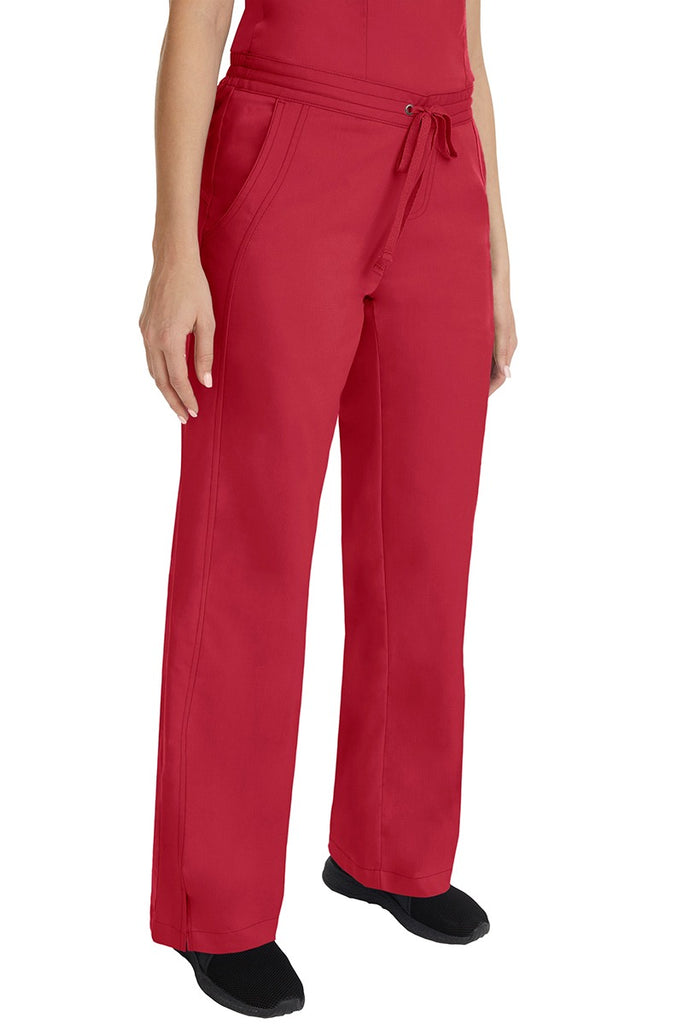 A young female RN wearing the Purple Label Women's Taylor Drawstring Scrub Pant in Red featuring side slits at the ankle for easy slip-on or removal.