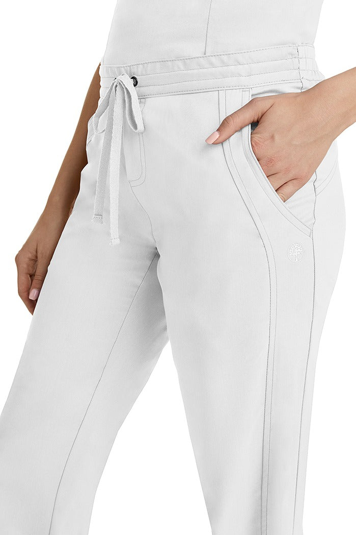 A young woman wearing a pair of Purple Label Women's Taylor Drawstring Scrub Pants from Healing Hands in White. Perfect for Healthcare Professionals working in Hospitals, Doctors offices, Dental Groups & Veterinary offices!