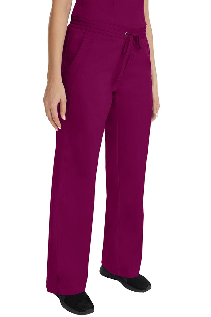 A young female RN wearing the Purple Label Women's Taylor Drawstring Scrub Pant in Wine featuring side slits at the ankle for easy slip-on or removal.