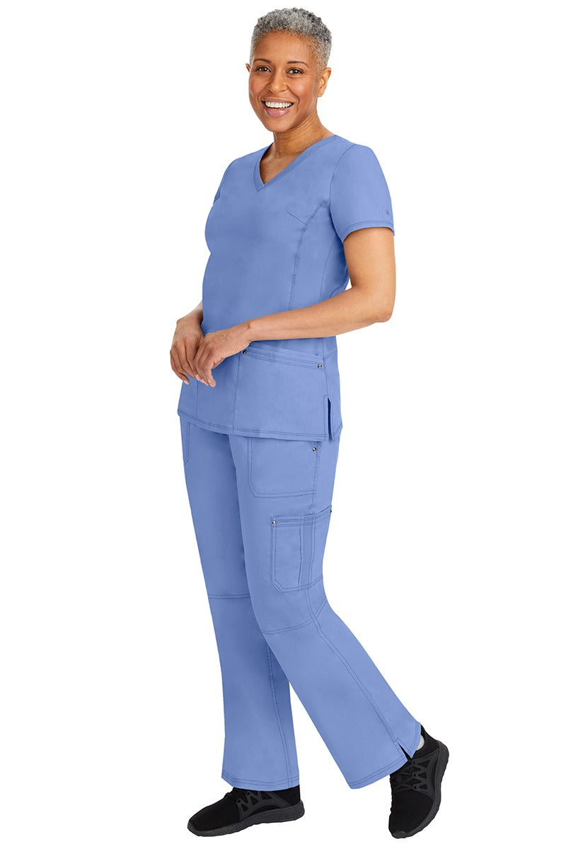 A young female nurse wearing a pair of Purple Label Women's Tori Yoga Waistband Scrub Pants from Healing Hands in Ceil featuring a modern fit.