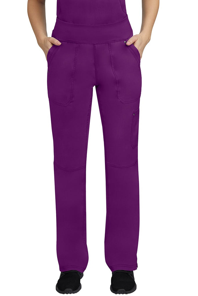 A young female LPN wearing a Purple Label Women's Tori Yoga Waistband Scrub Pant in Eggplant featuring 2 front side-entry pockets with grommet details.