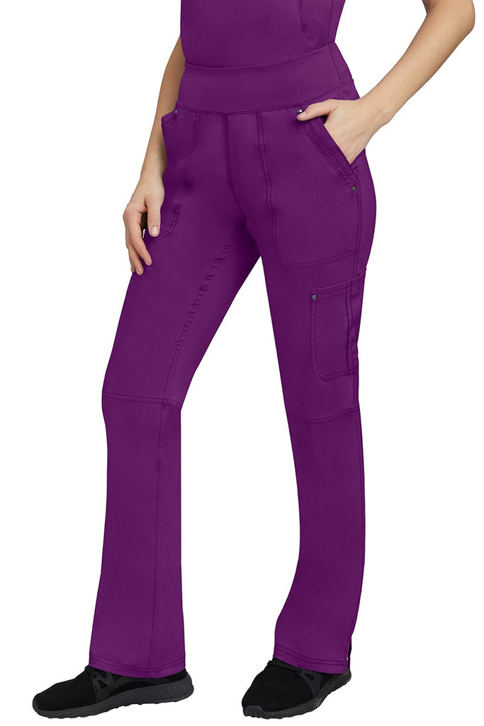 A young Home Care Registered Nurse wearing a pair of Purple Label Women's Tori Yoga Waistband Scrub Pants in Eggplant featuring 1 outer cargo pocket on the wearer's left side pant leg.