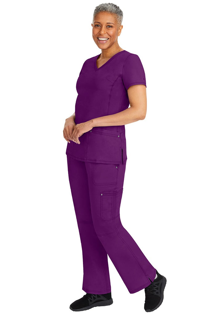 A young female nurse wearing a pair of Purple Label Women's Tori Yoga Waistband Scrub Pants from Healing Hands in Eggplant featuring a modern fit.