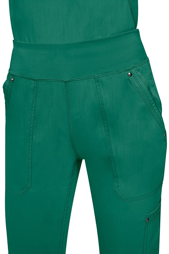 A young female healthcare professional wearing a Purple Label Women's Tori Yoga Waistband Scrub Pant in Hunter Green featuring a unique fabric that resists wrinkles, shrinking, & fading better than traditional cotton scrubs.