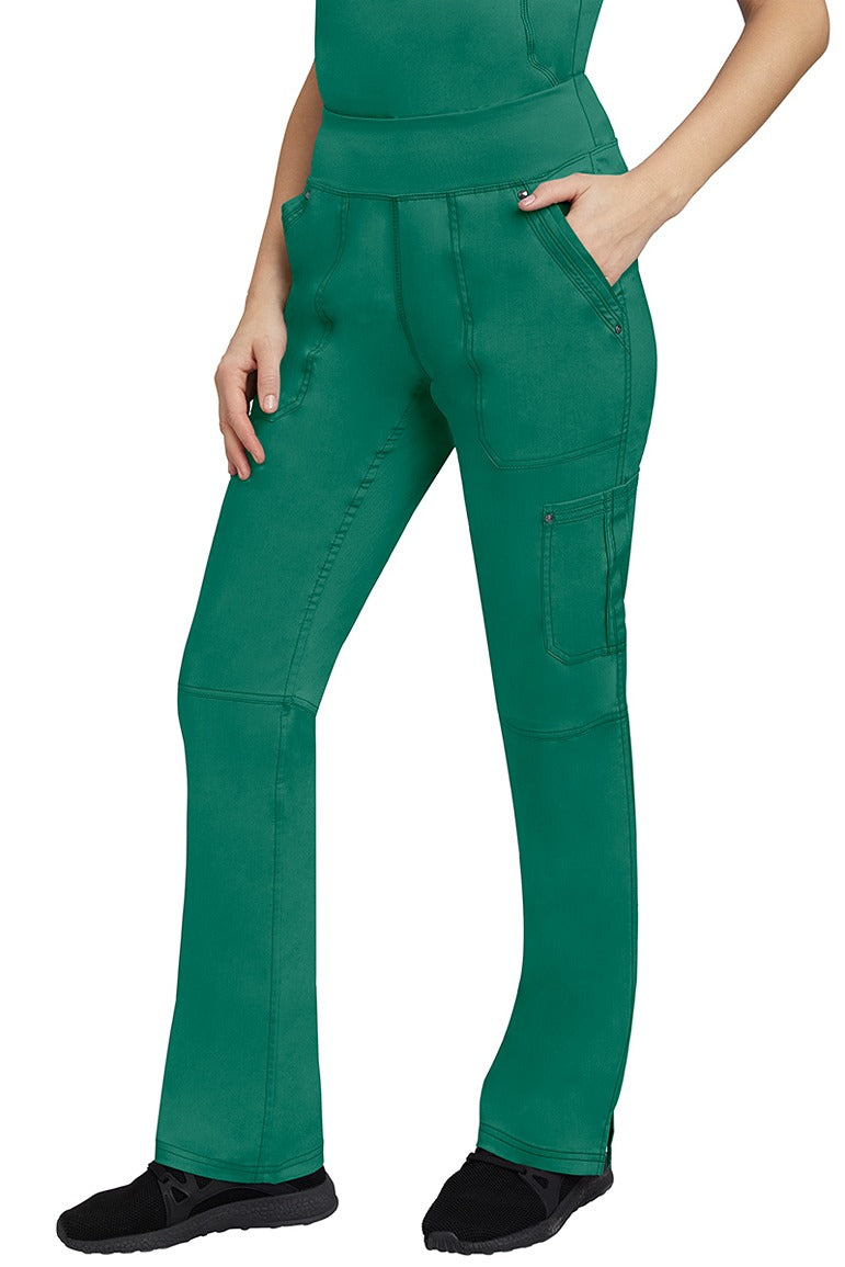 A young Home Care Registered Nurse wearing a pair of Purple Label Women's Tori Yoga Waistband Scrub Pants in Hunter Green featuring 1 outer cargo pocket on the wearer's left side pant leg.