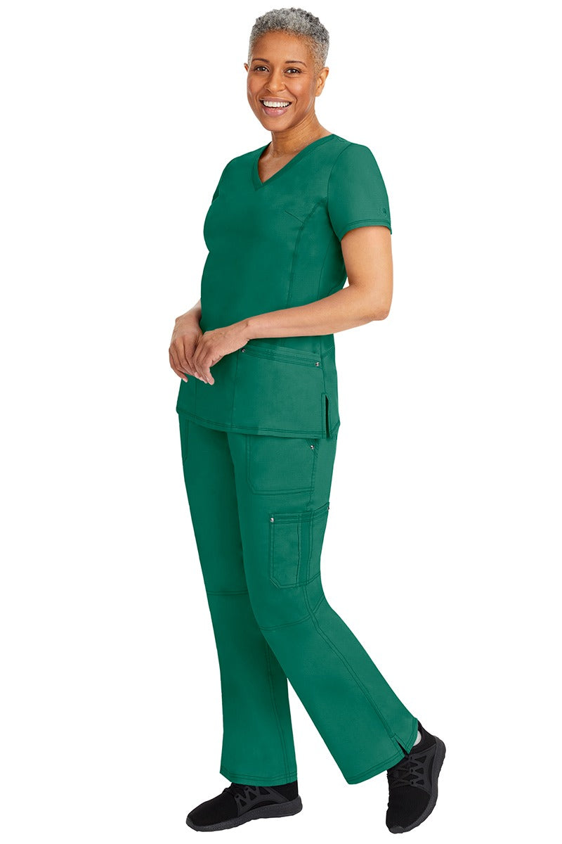 A young female nurse wearing a pair of Purple Label Women's Tori Yoga Waistband Scrub Pants from Healing Hands in Hunter Green featuring a modern fit.