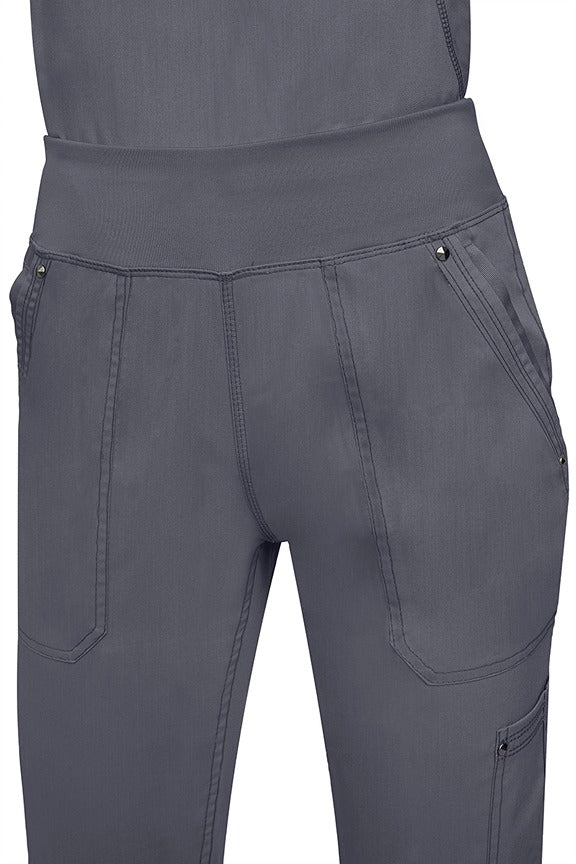 A young female healthcare professional wearing a Purple Label Women's Tori Yoga Waistband Scrub Pant in Pewter featuring a unique fabric that resists wrinkles, shrinking, & fading better than traditional cotton scrubs.