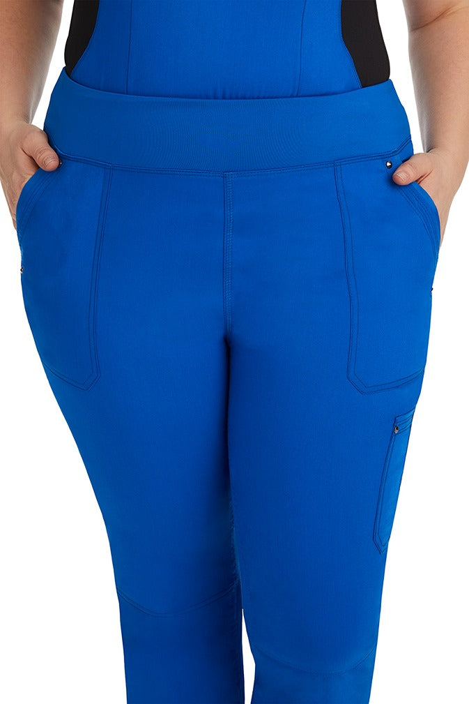 A young female healthcare professional wearing a Purple Label Women's Tori Yoga Waistband Scrub Pant in Royal featuring a unique fabric that resists wrinkles, shrinking, & fading better than traditional cotton scrubs.