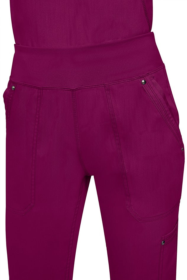 A young female healthcare professional wearing a Purple Label Women's Tori Yoga Waistband Scrub Pant in Wine featuring a unique fabric that resists wrinkles, shrinking, & fading better than traditional cotton scrubs.
