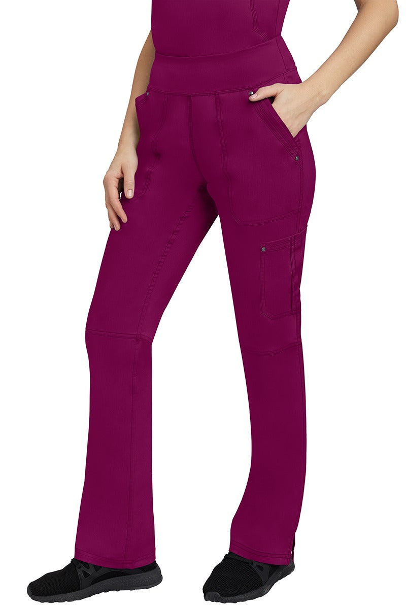 A young Home Care Registered Nurse wearing a pair of Purple Label Women's Tori Yoga Waistband Scrub Pants in Wine featuring 1 outer cargo pocket on the wearer's left side pant leg.