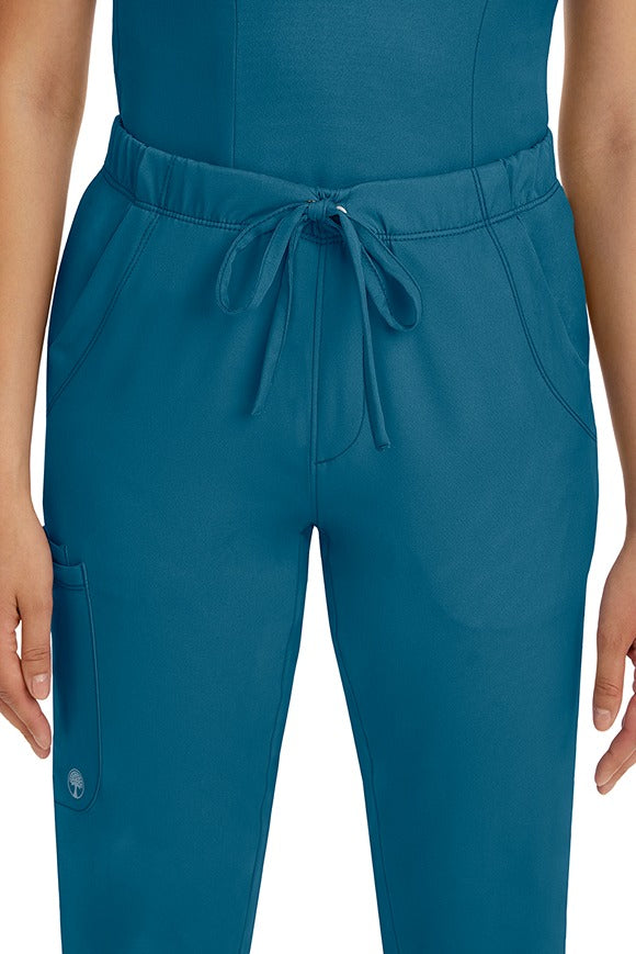 A female LPN wearing a pair of HH-Works Women's Rebecca Multi-Pocket Drawstring Pants in Caribbean featuring 2 front slip pockets with a cargo pocket at the wearer's right leg.