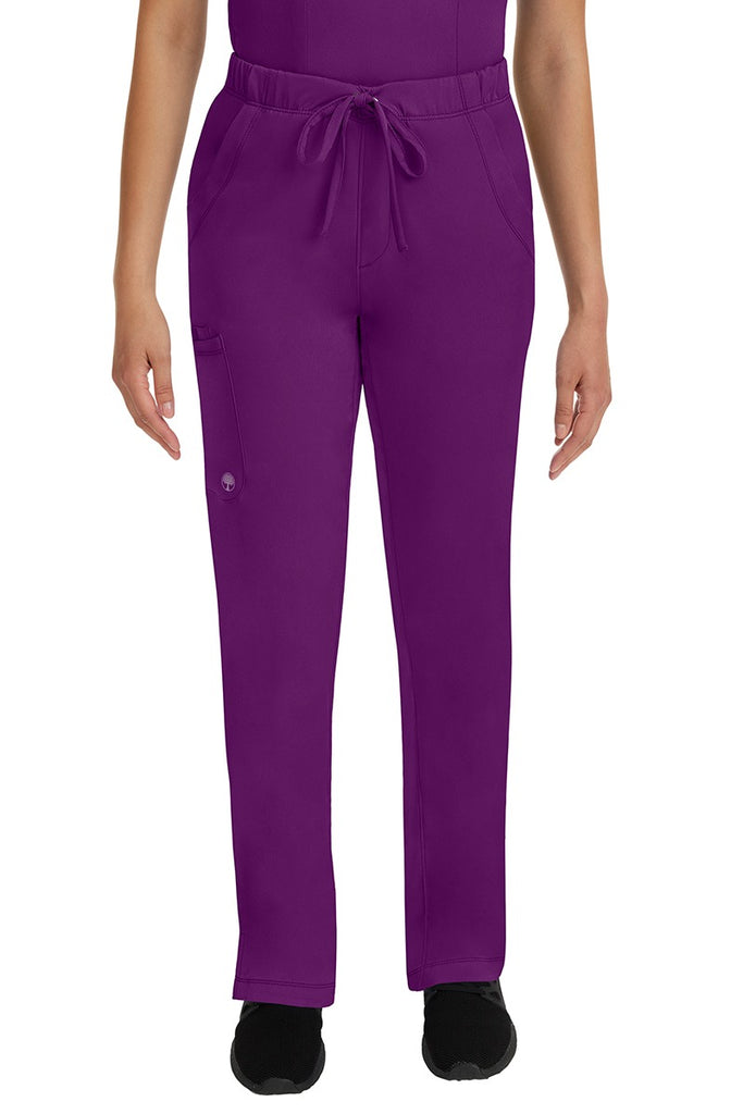 A young lady LPN wearing an HH Works Women's Rebecca Multi-Pocket Drawstring Pant in Eggplant featuring n all elastic waistband with a drawstring tie front.